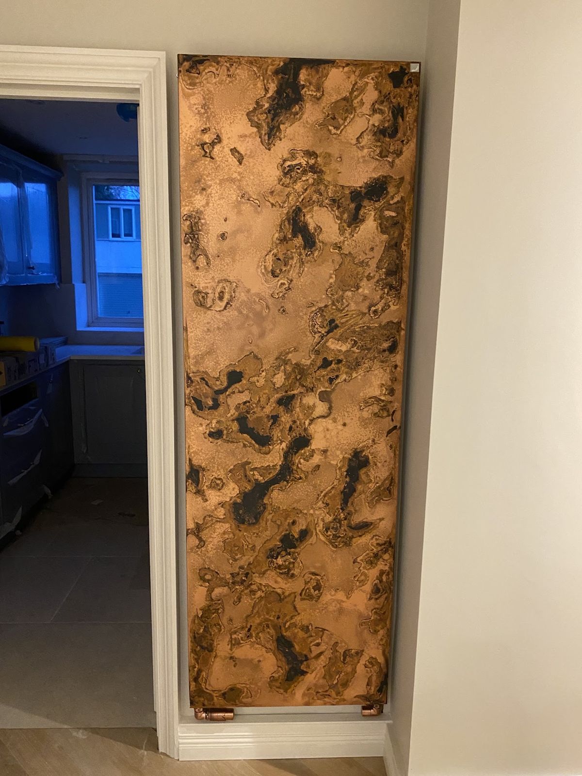 Tall copper-finish designer radiator on a hallway wall