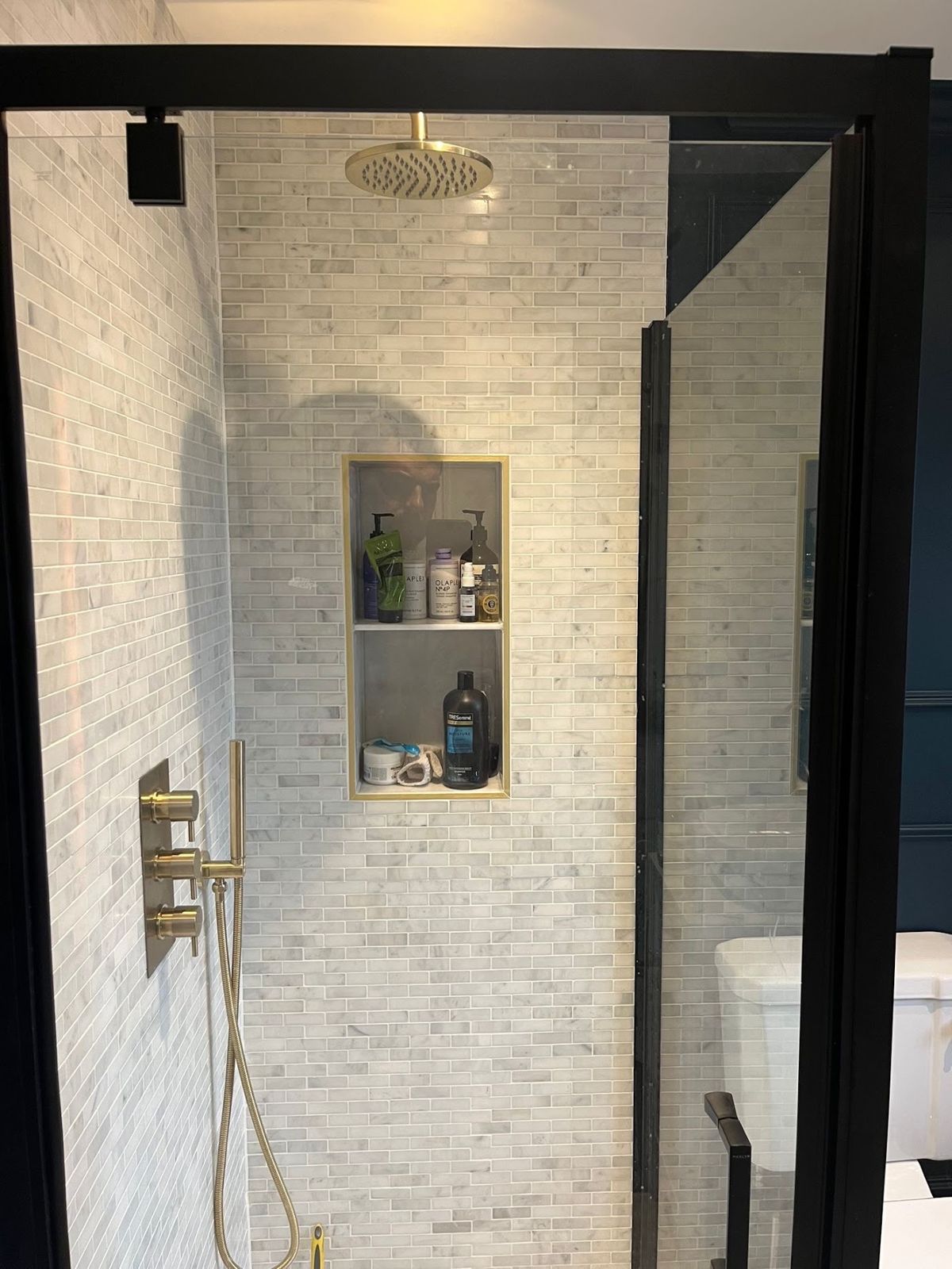 Walk-in shower with marble mosaic tiles, brass fittings and a recessed shelf
