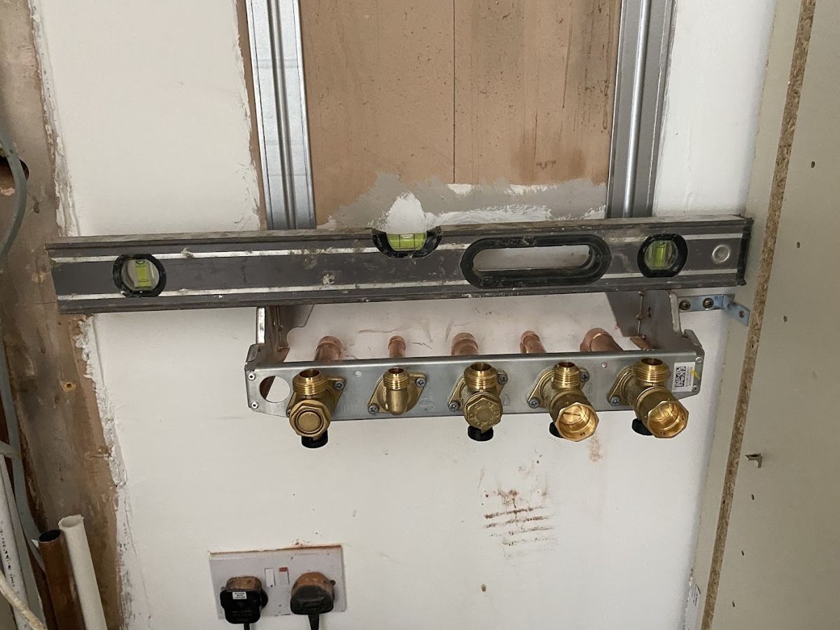 Brass shower valve manifold fixed inside a wall with a spirit level resting above it