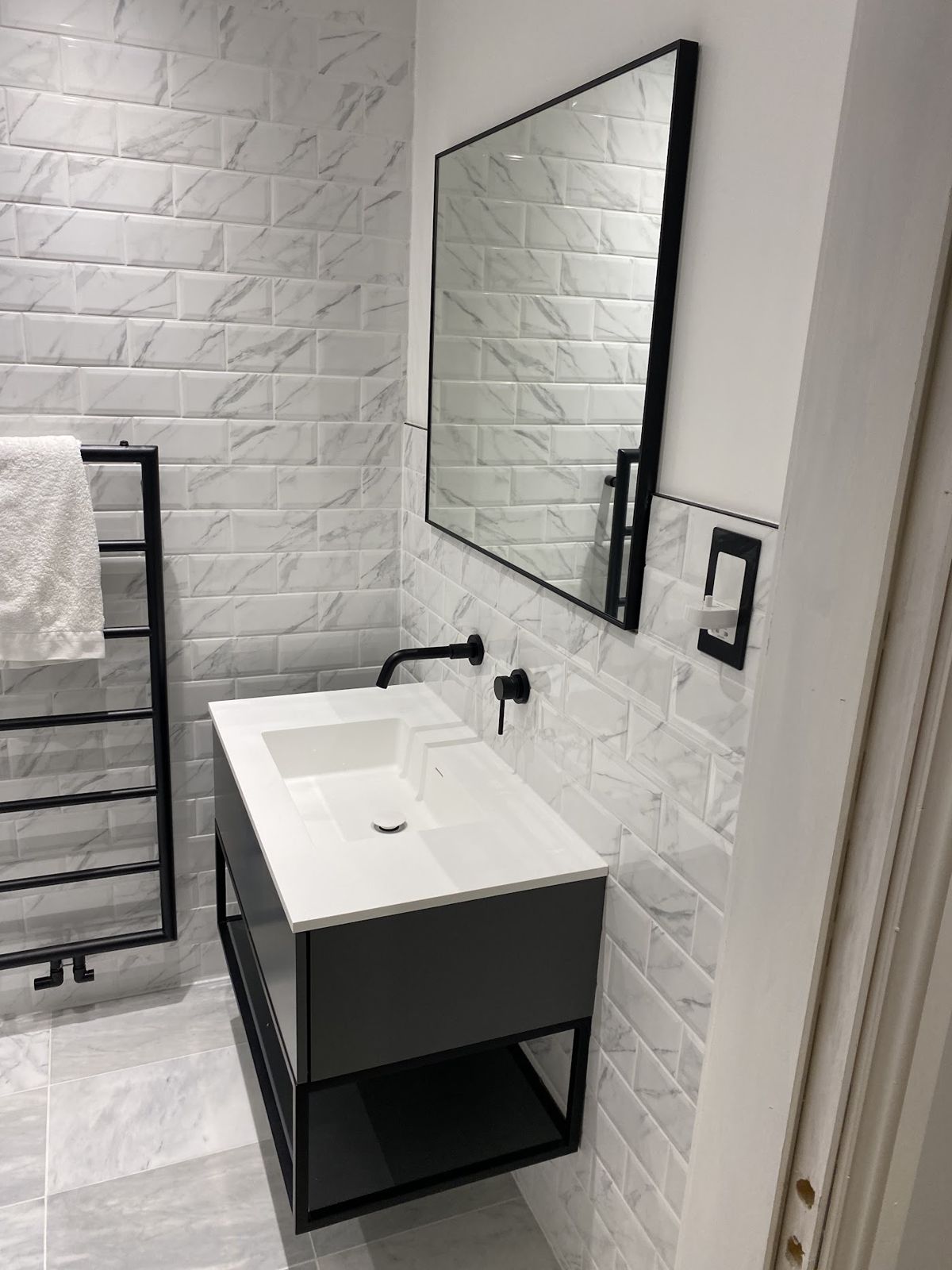 Bathroom vanity with black tap and mirror against white metro tiles